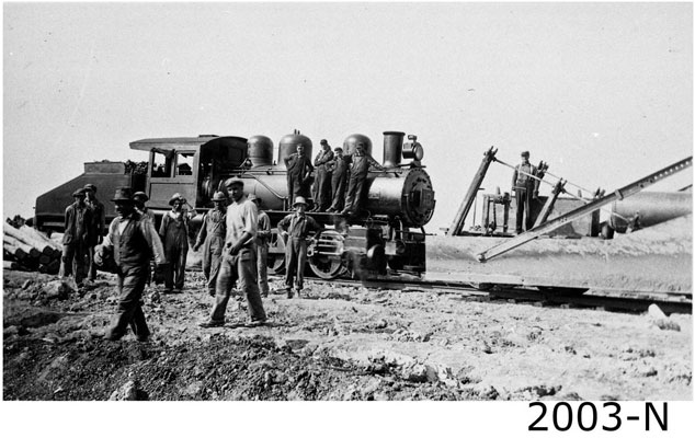 <p>The Welland Canal Construction Railway was the Canal corridor’s backbone. It enabled all work to take place hauling in equipment, hauling away debris, and at times pressed into service to convey an injured worker to the Homer Hospital. A dozen workers with their grinning boss in foreground take a welcomed break from the hard labour to pose for a photo. Photo attribution: St. Catharines Museum - Claude Richardson Collection - 1970.1.35</p>