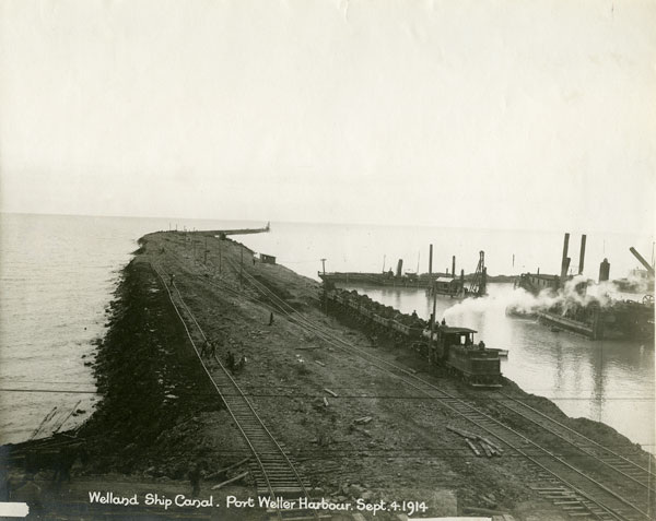<p>This image shows the Port Weller construction site in September 1914. A large quantity of earth and rock was used to fill concrete cribs that were sunk into the lake to build the piers for the Welland Ship Canal. Photo attribution: St. Catharines Museum – 1340-N</p>